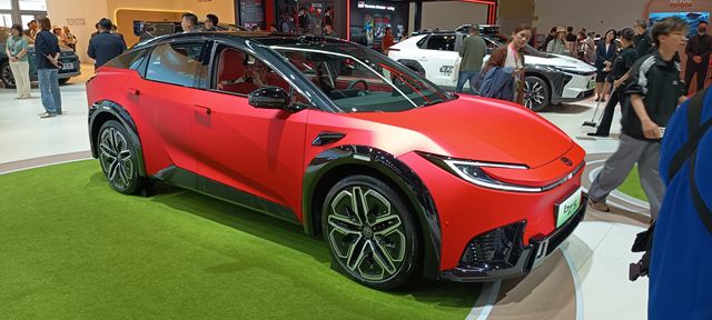 Carro elétrico vermelho em exposição em um evento automobilístico, com visitantes ao fundo.