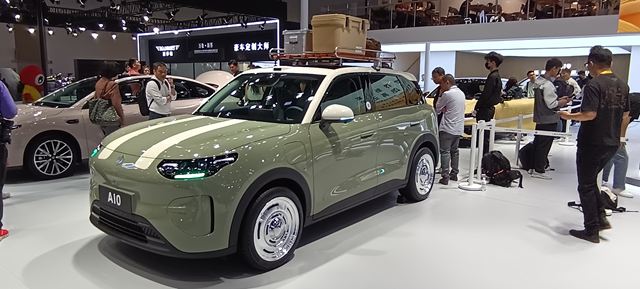 Um carro SUV de cor verde com listras brancas, exibido em um evento automotivo, cercado por pessoas e câmeras.