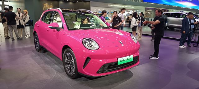 Carro rosa em uma exposição, com visitantes ao fundo.