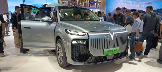 SUV prateada exposição em evento automobilístico, com porta aberta e diversas pessoas ao redor.