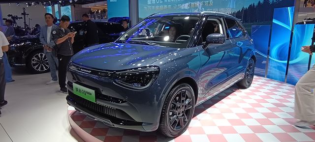 SUV moderno em exposição com pintura cinza e rodas esportivas, cercado por visitantes em um evento automotivo.