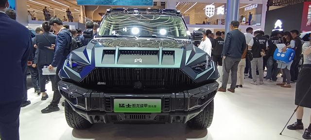 Imagem de um veículo robusto com design agressivo, exibido em uma feira automotiva, cercado por espectadores.