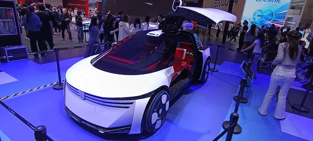 Um carro futurista e elegante em uma exposição, com design branco e detalhes vermelhos, cercado por um público interessado.