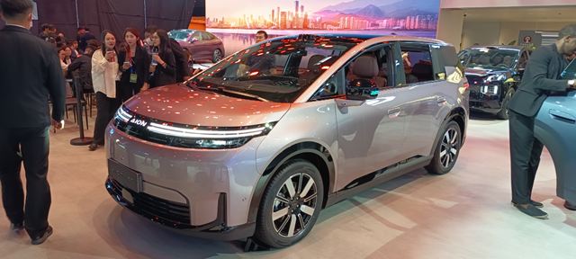 Um carro elétrico moderno em uma exposição, com um design sleek e contemporâneo, exibido em um ambiente iluminado.