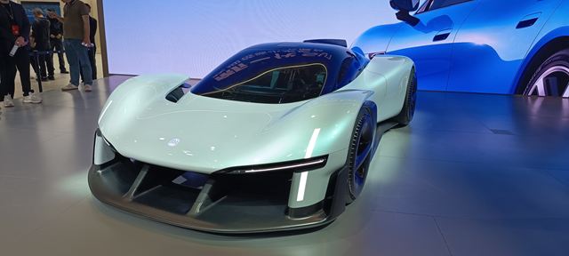 Carro esportivo futurista em exibição, com design aerodinâmico e pintura clara, em um ambiente moderno.