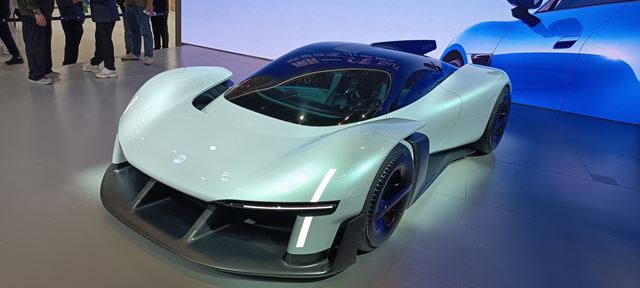 Carro esportivo futurista com design aerodinâmico, pintura azul clara e rodas pretas, exibido em um evento automobilístico.