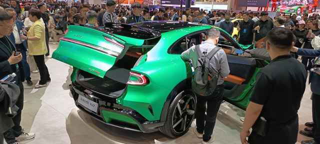 Um carro esportivo verde com porta traseira aberta, cercado por uma multidão em um evento, exibindo seu design moderno e interior.