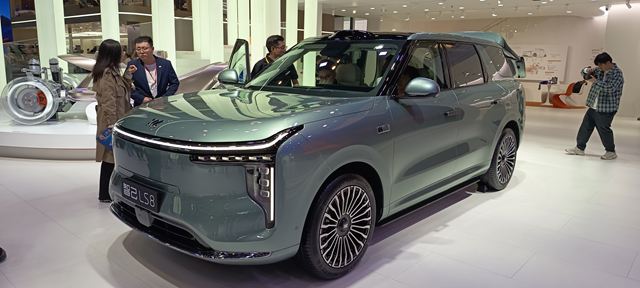 Um SUV moderno em exibição em um evento, com design inovador e elegante, rodeado por pessoas que o admiram.