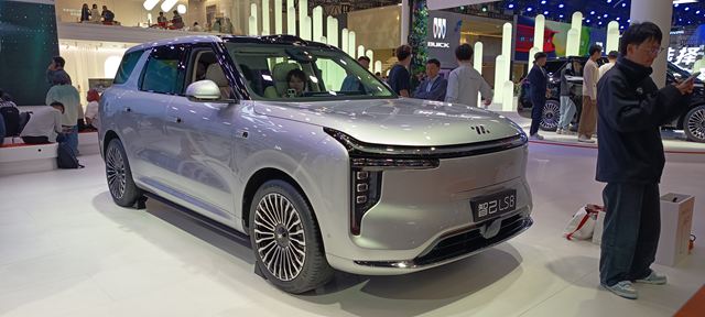 Um SUV prateado em um evento automotivo, exibindo design moderno e rodas detalhadas.