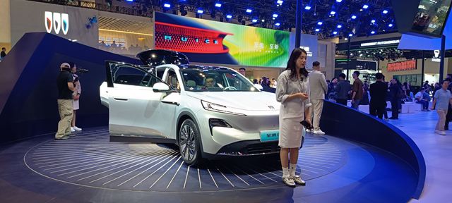 Exposição de um carro elétrico em um evento, com uma mulher apresentando ao lado do veículo em um ambiente moderno e iluminado.