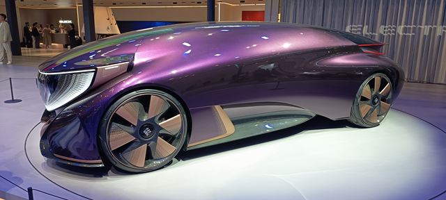Carro conceito futurista em tonalidade roxa, com design aerodinâmico e rodas estilizadas, exibido em um evento de tecnologia.