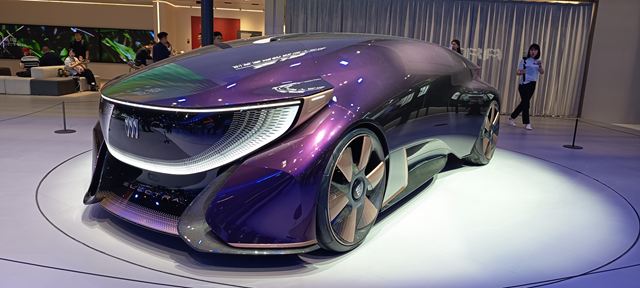 Um carro conceitual futurista com design elegante e cores roxas, exibido em um ambiente moderno.