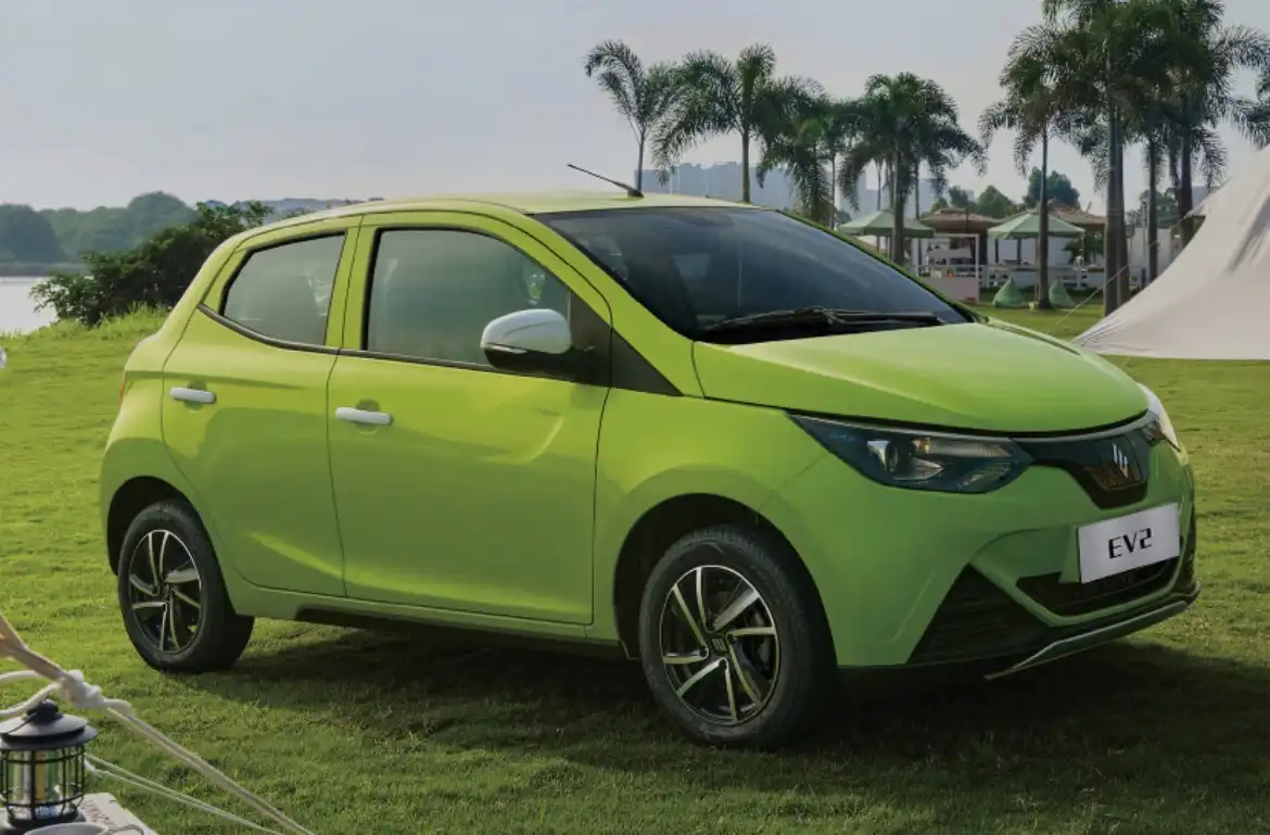 Um carro elétrico compacto verde em um ambiente ao ar livre com palmeiras ao fundo.