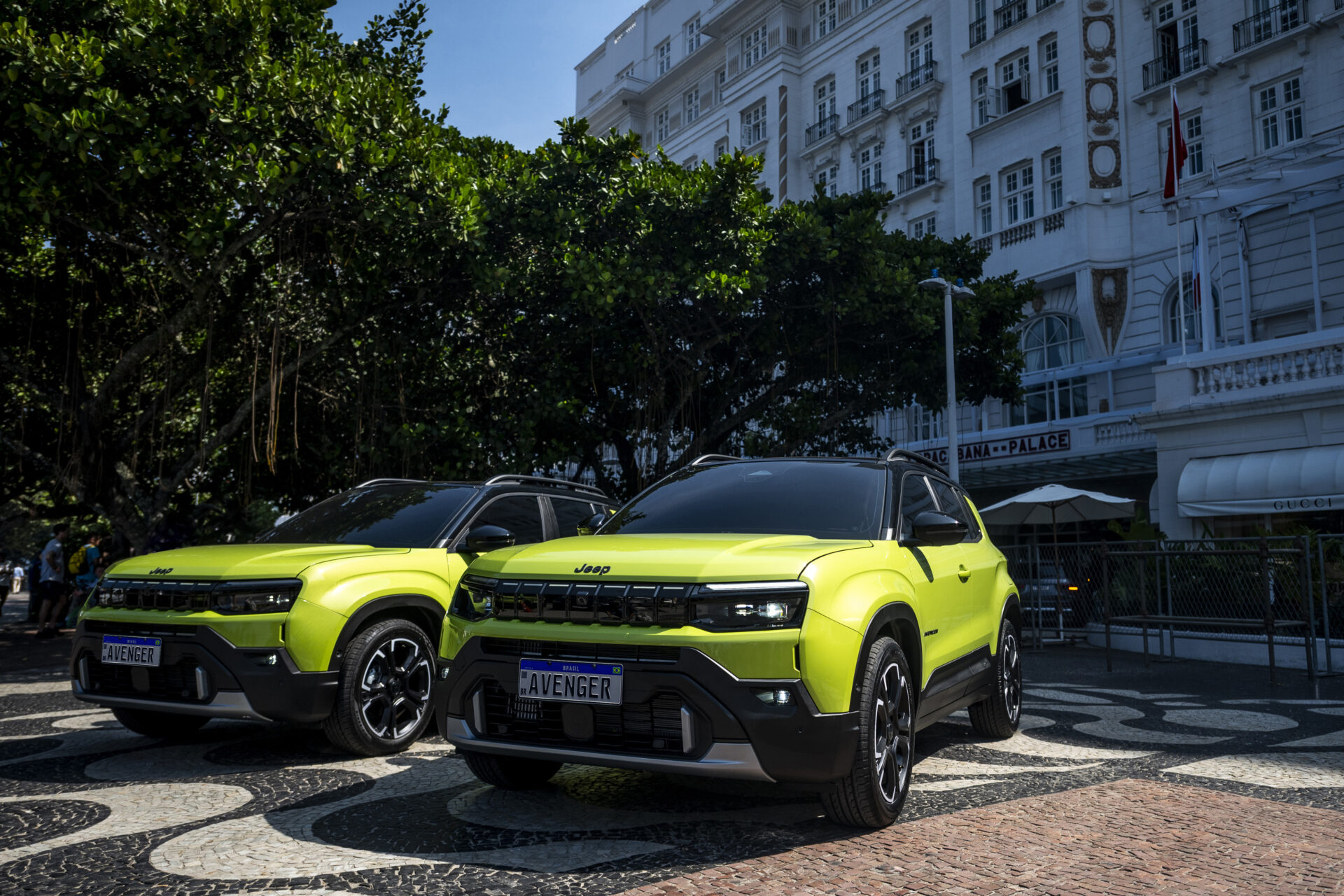 Dois SUVs Jeep Avenger de cor verde-limão estacionados em uma calçada decorada, com um edifício histórico ao fundo.