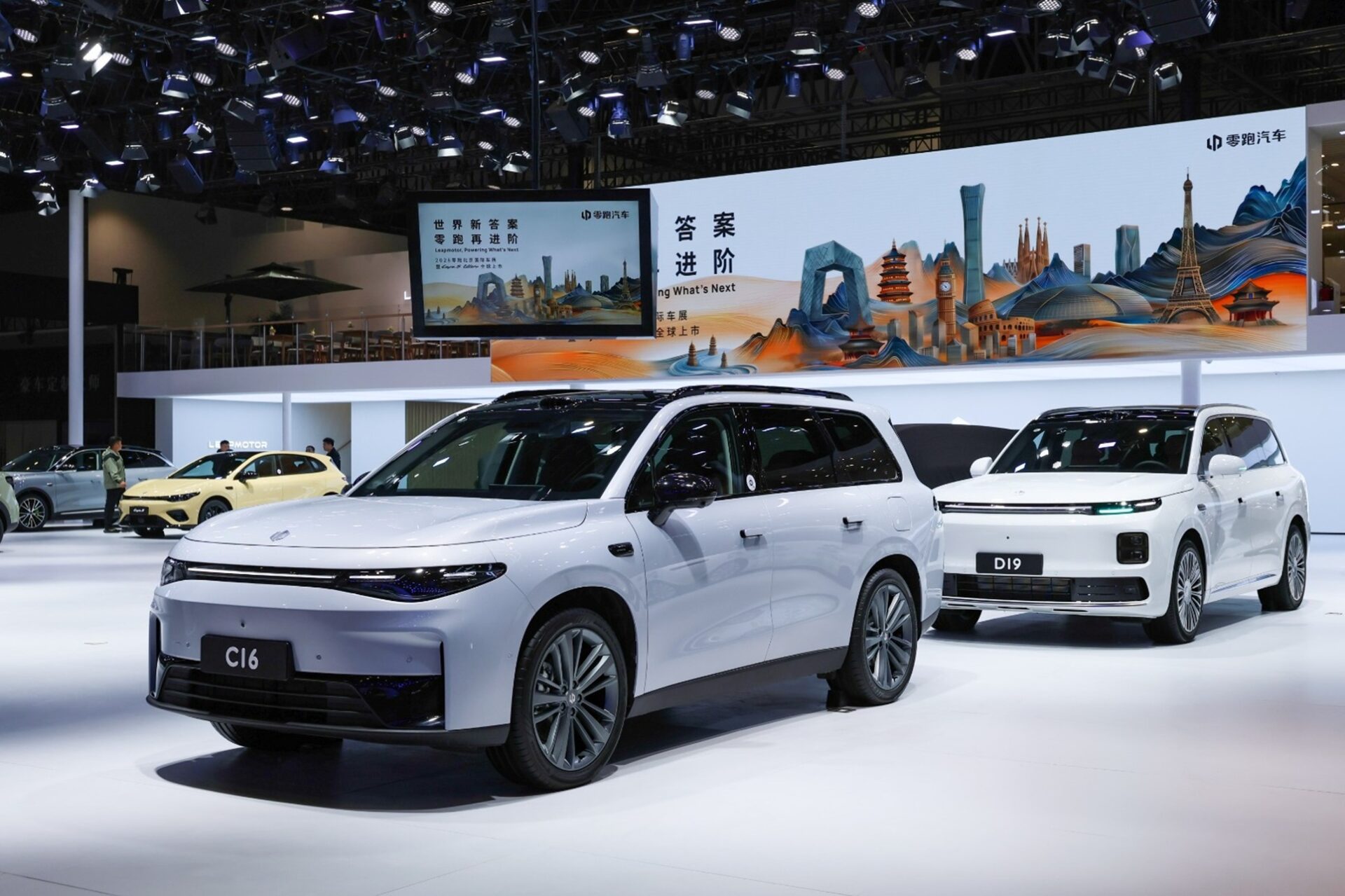 Two modern SUVs on display at an automotive show, featuring a sleek white C16 model in the foreground and a white D19 model in the background, with a colorful cityscape backdrop.