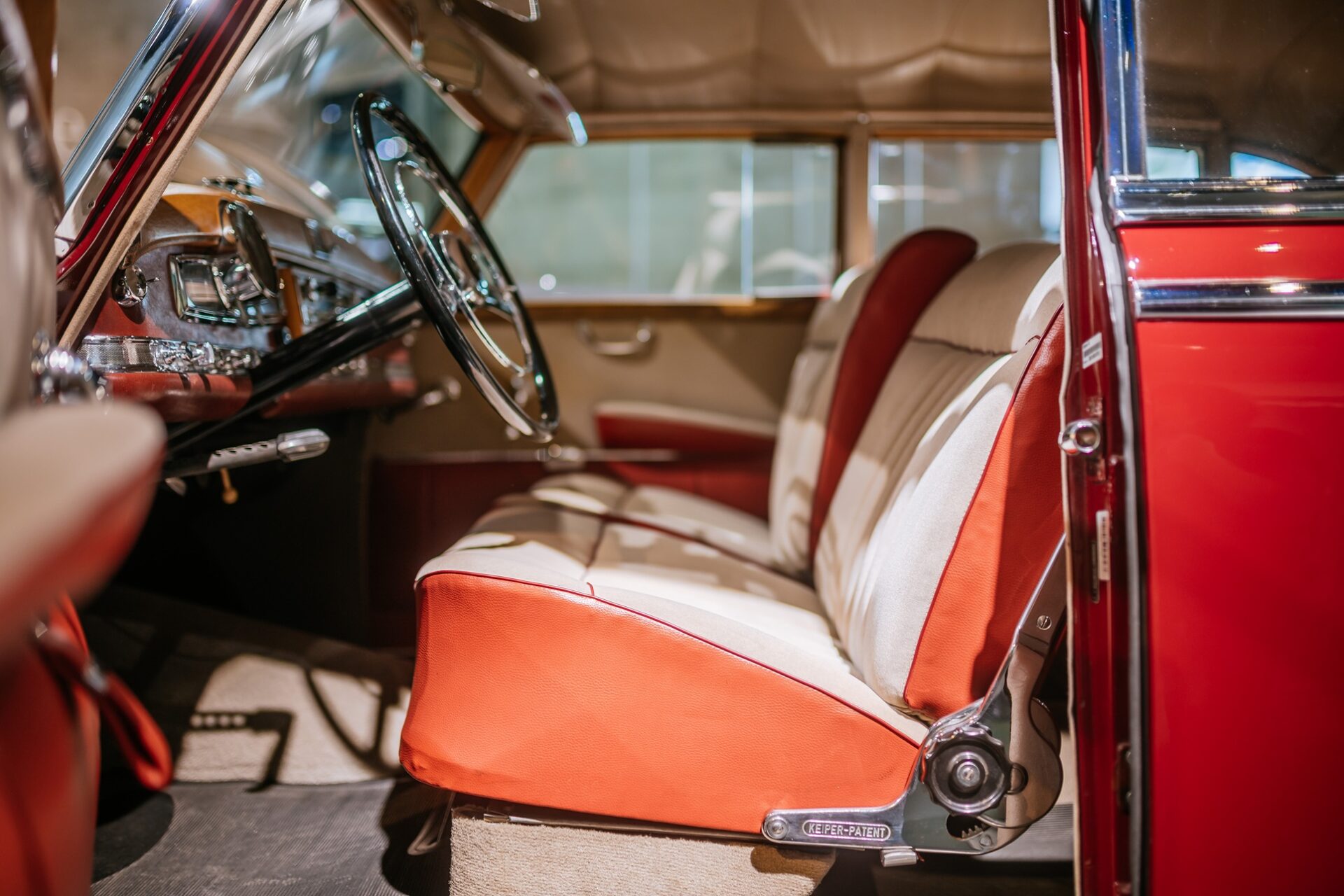 Interior view of a vintage car showing leather seats in orange and cream colors, a chrome steering wheel, and dashboard details.
