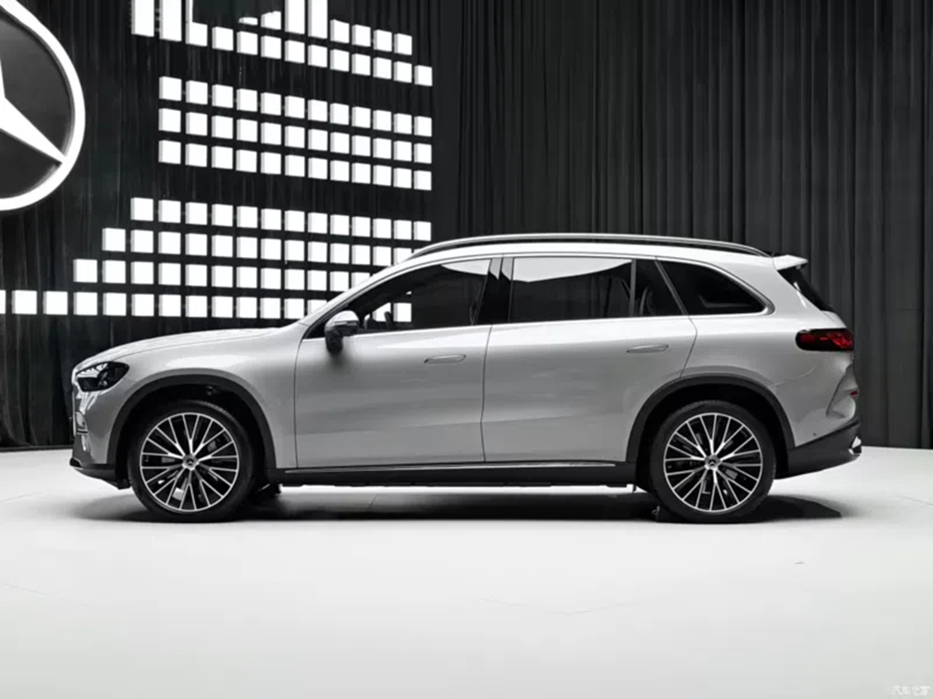 Side view of a silver luxury SUV on a minimalist stage with a dark backdrop and illuminated geometric patterns.