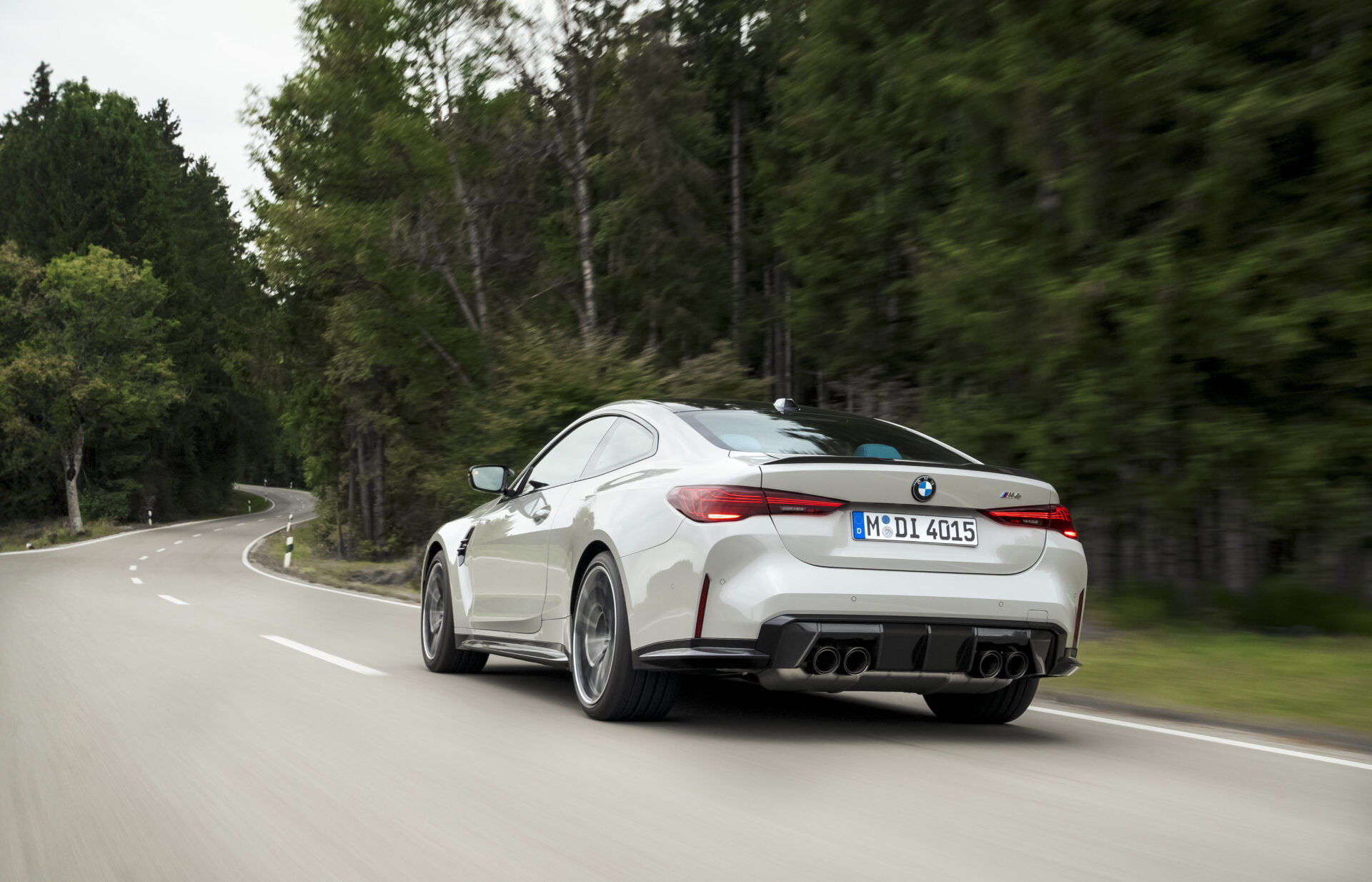 Um BMW M4 branco em movimento numa estrada sinuosa cercada por árvores.