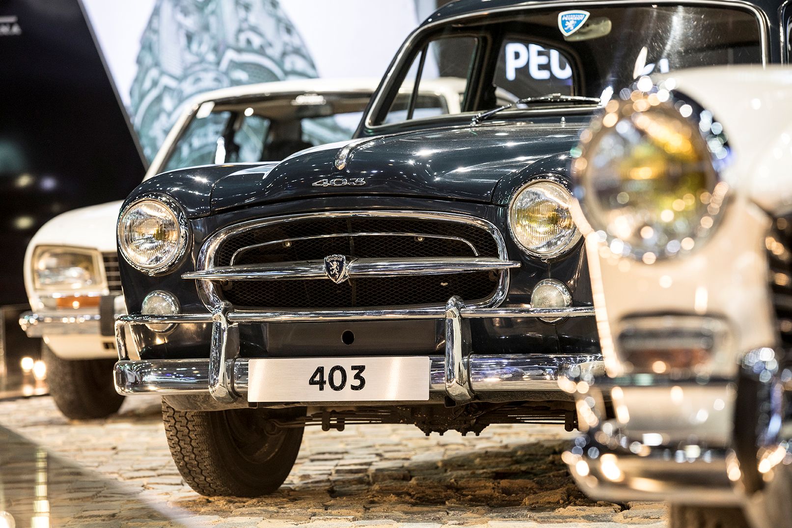 Detalhe de carros clássicos em um evento automotivo, incluindo um Peugeot 403 em primeiro plano.