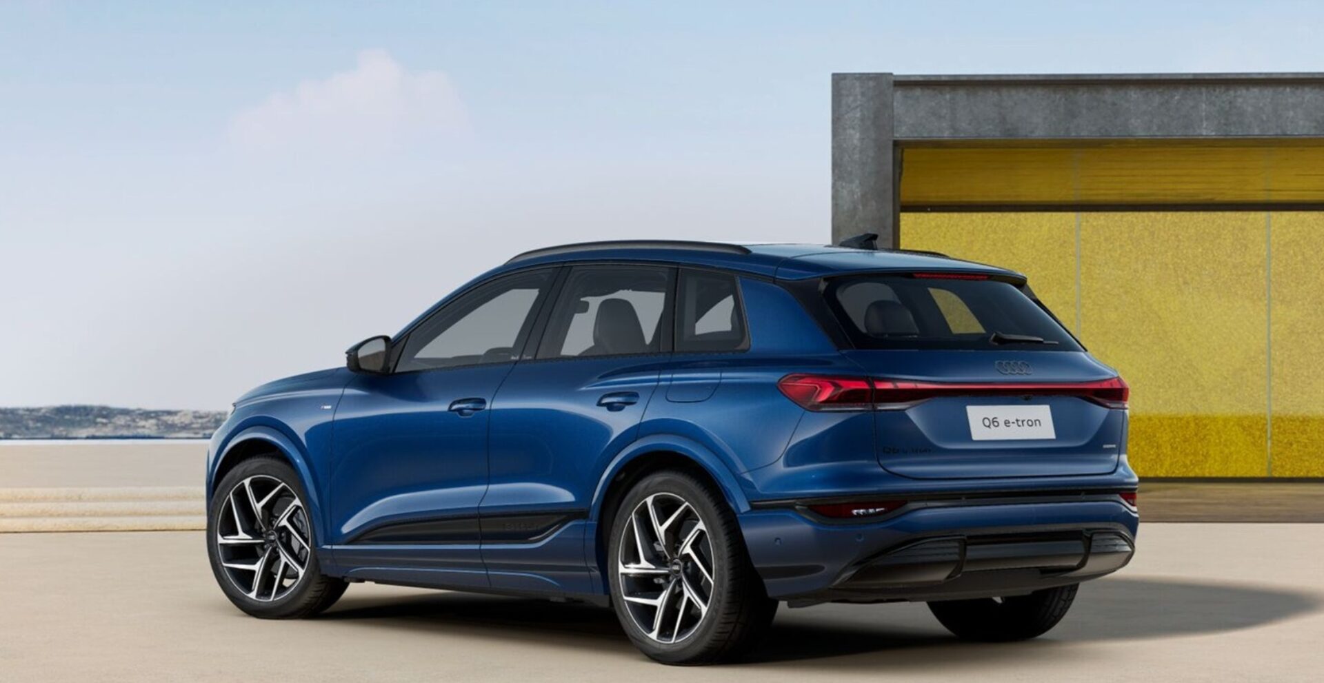 A blue Audi Q6 e-tron showcased from a rear angle with modern architecture in the background.