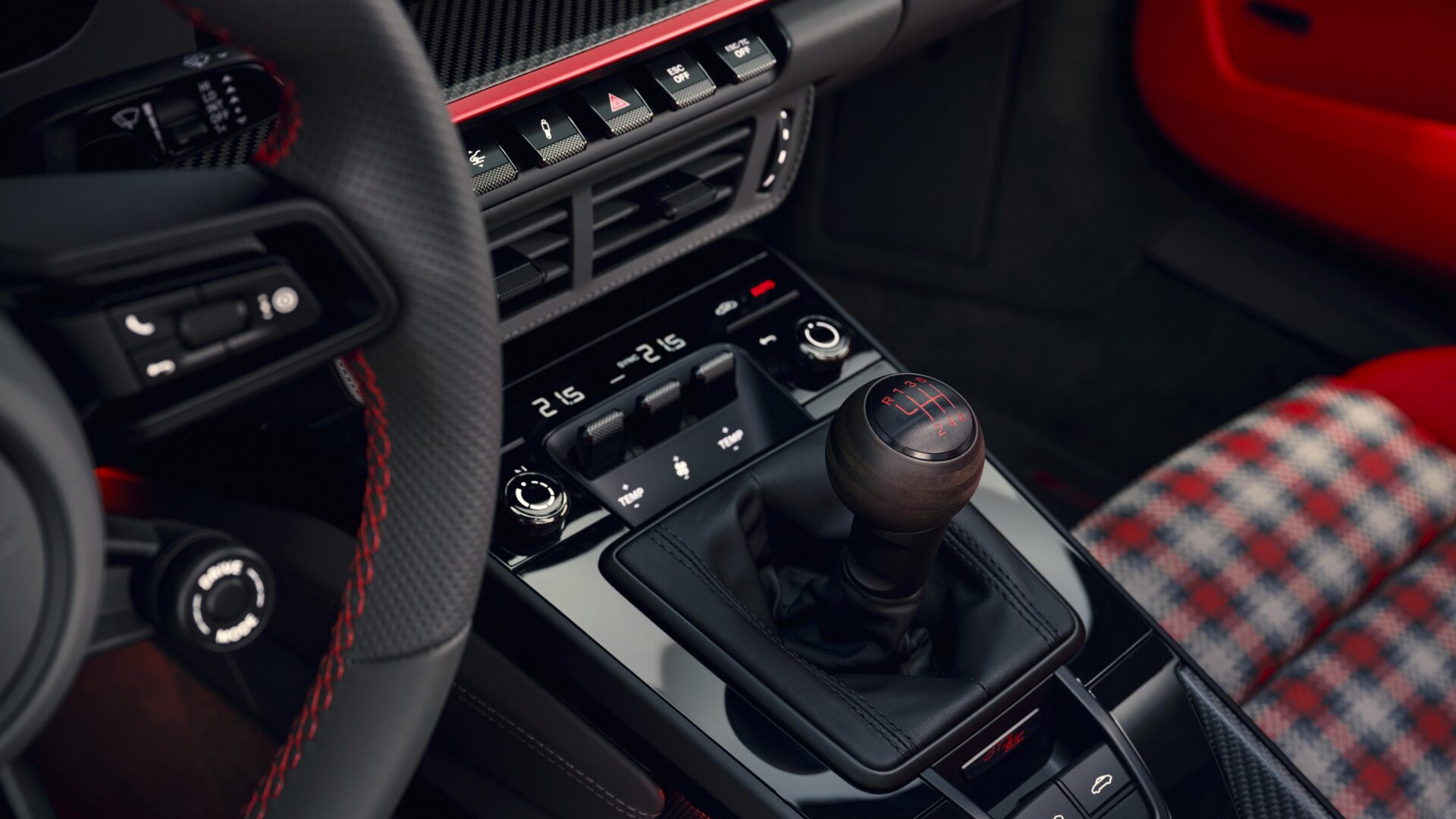 Interior de carro com foco na alavanca de câmbio manual e painel de controle com detalhes em vermelho e preto.
