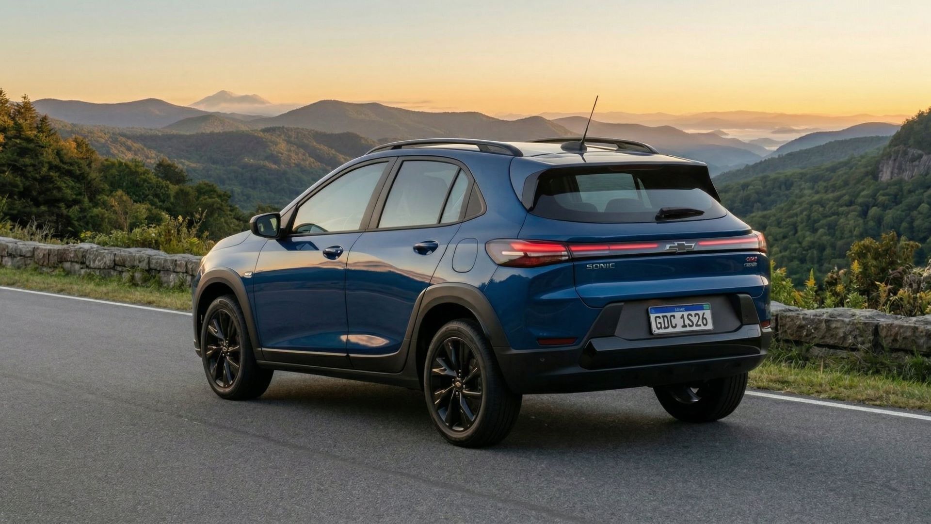 Um carro SUV azul estacionado em uma estrada, com montanhas e um céu alaranjado ao fundo.