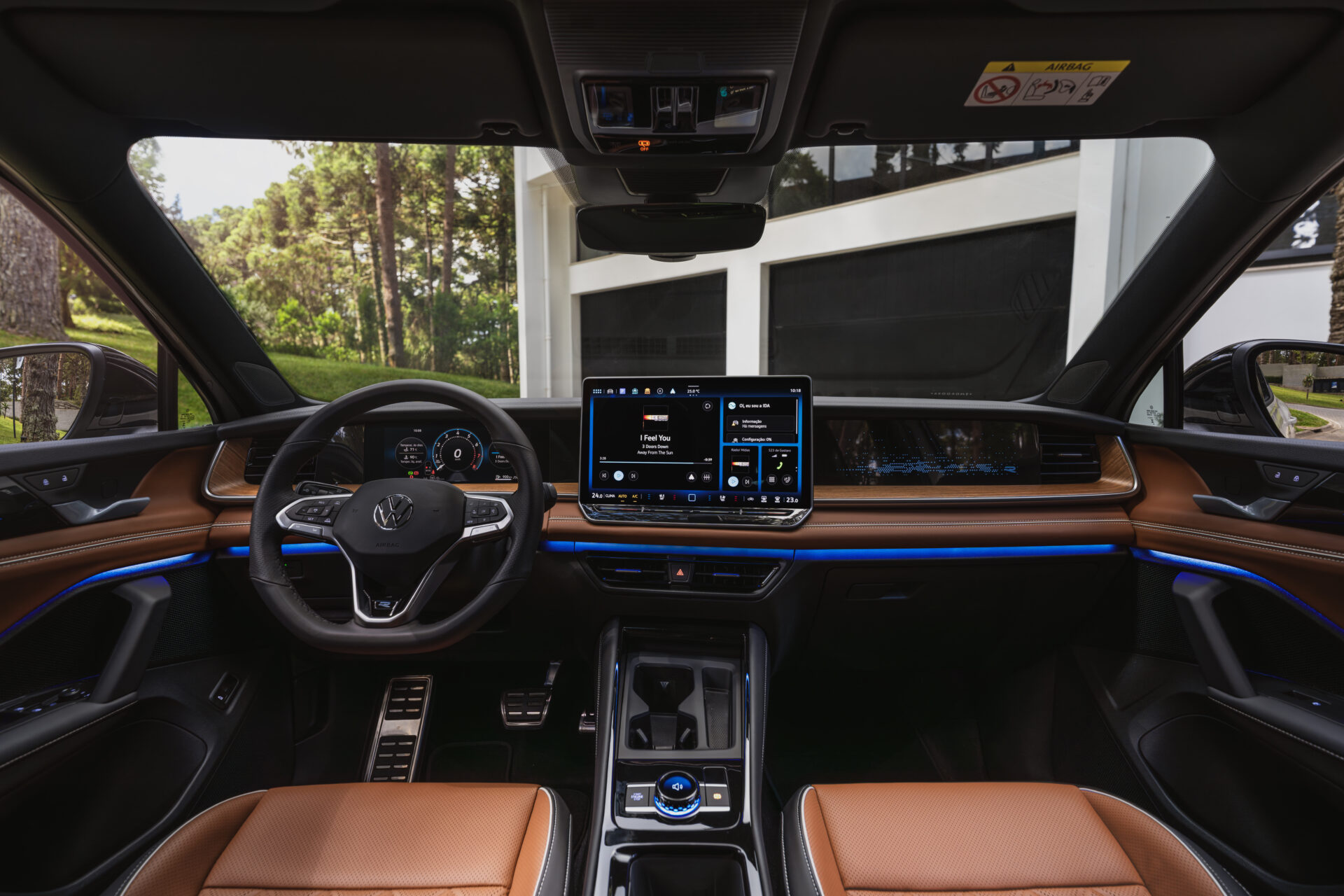 Imagem do interior de um carro Volkswagen, exibindo volante, painel digital e tela multimídia. O interior possui detalhes em couro marrom e iluminação em LED azul.