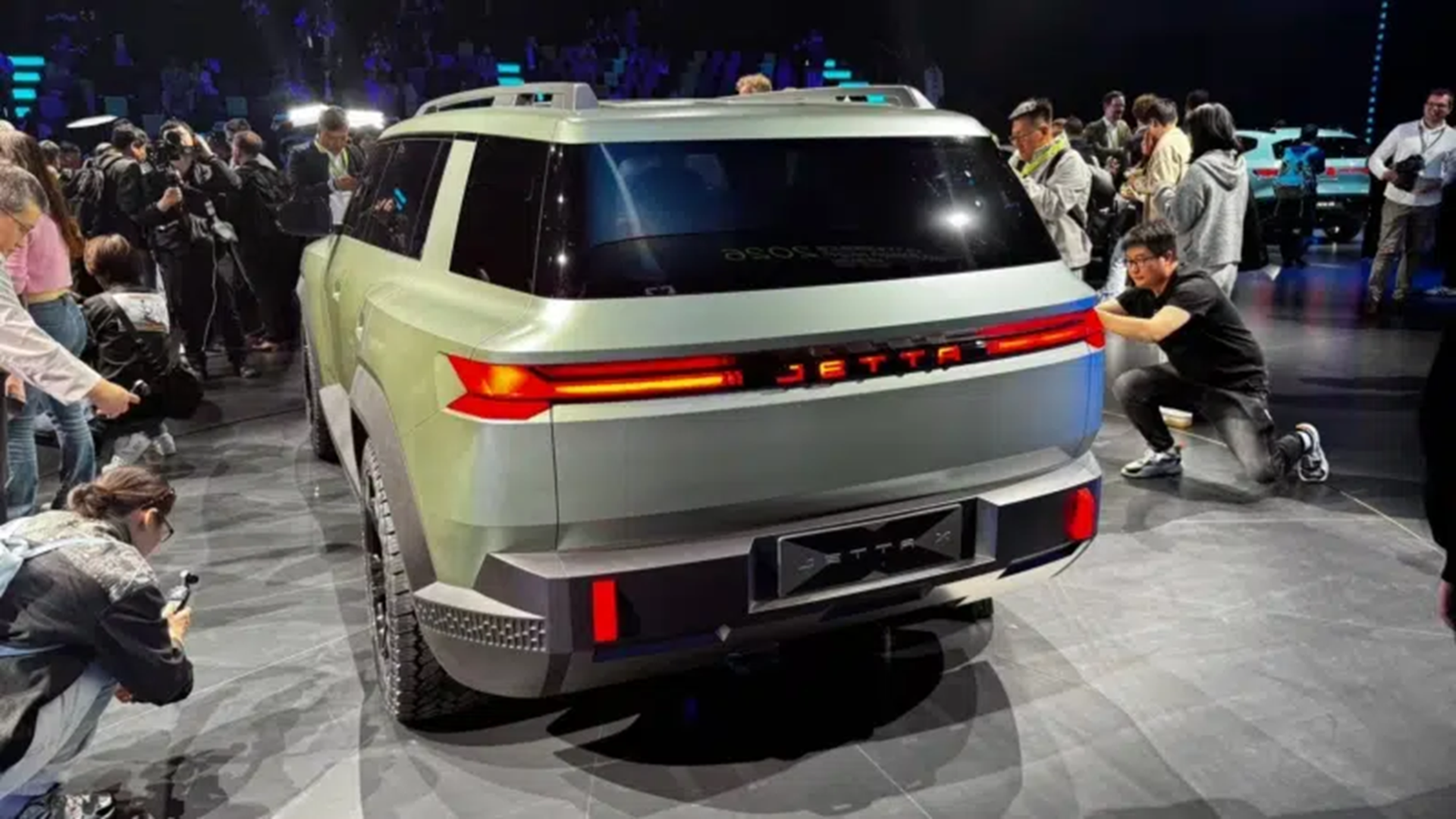 A new Jetta vehicle showcased at an event, viewed from the rear, surrounded by photographers and attendees capturing the launch.