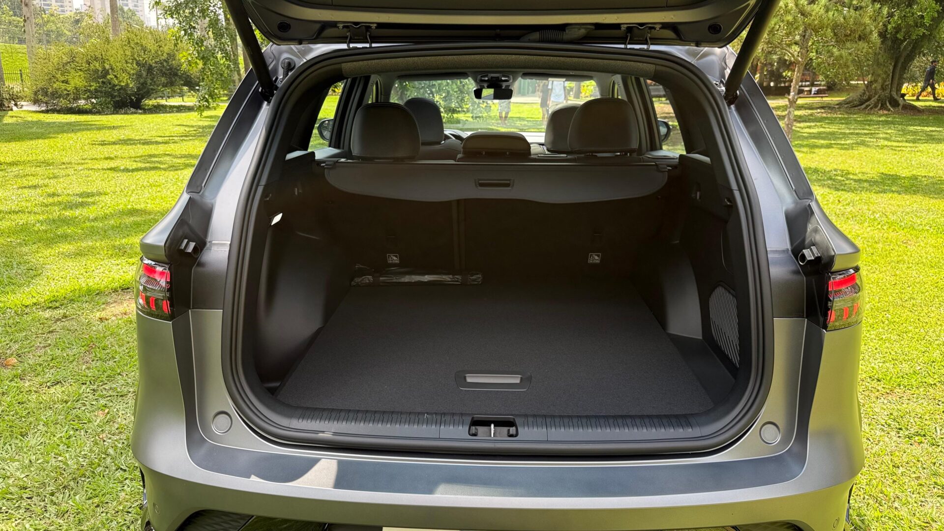 Bagageiro de um carro SUV mostrado de dentro, com o espaço vazio e a tampa levantada, em um ambiente ao ar livre com grama verde ao fundo.