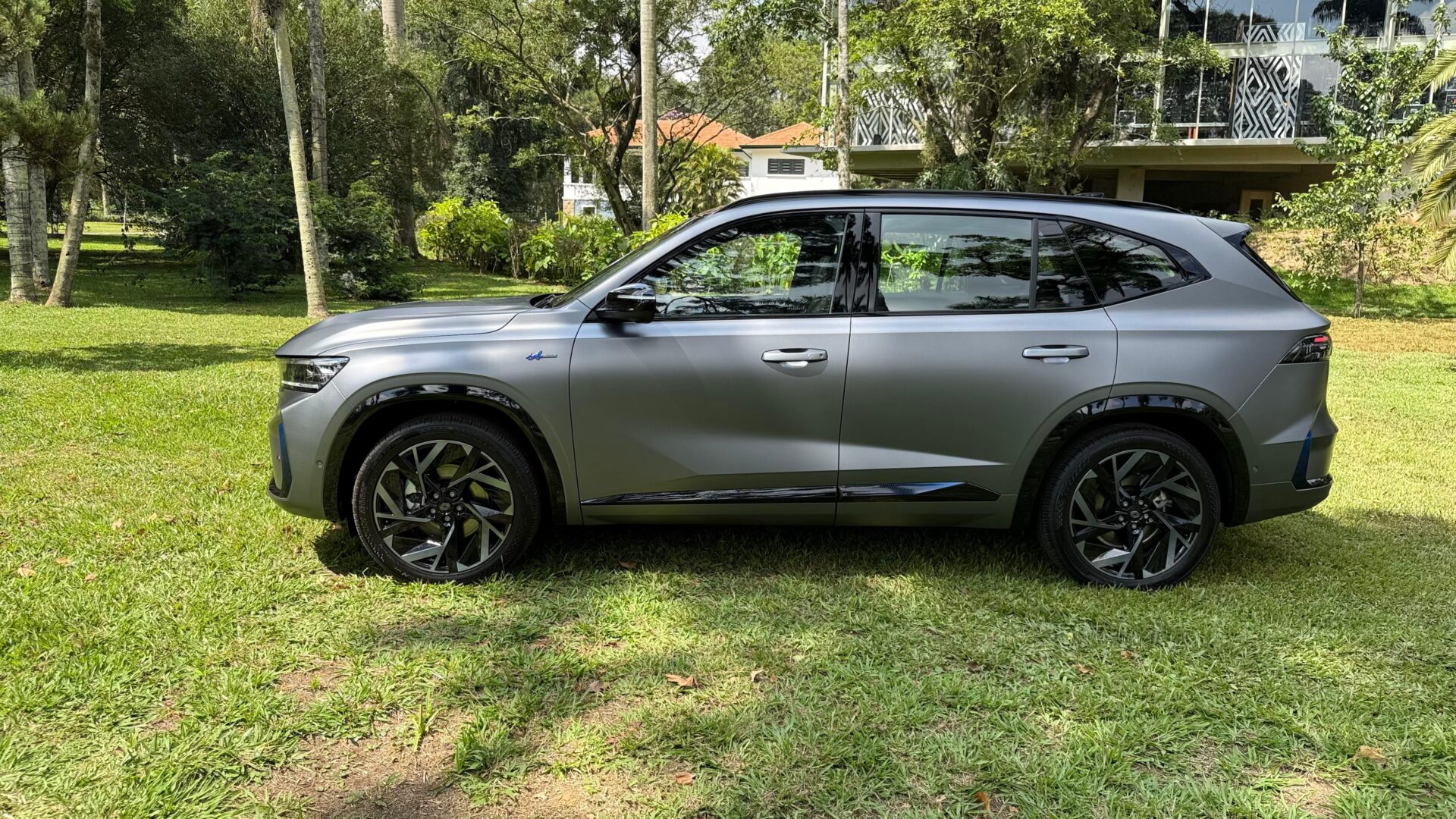 Um SUV cinza metálico estacionado em uma área verde, com árvores ao fundo.
