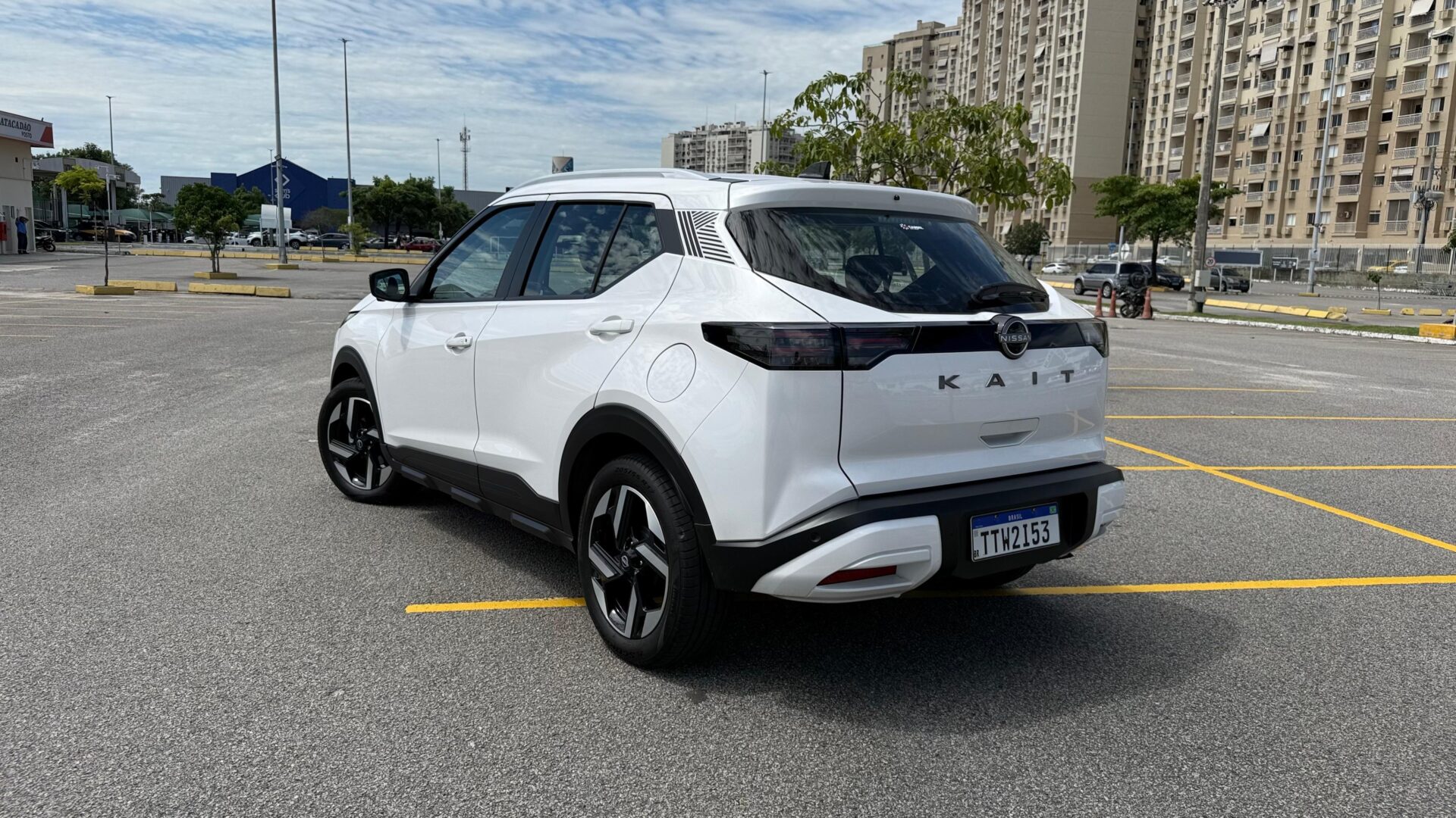 SUV branco estacionado em um estacionamento vazio, com edifícios ao fundo e céu nublado.