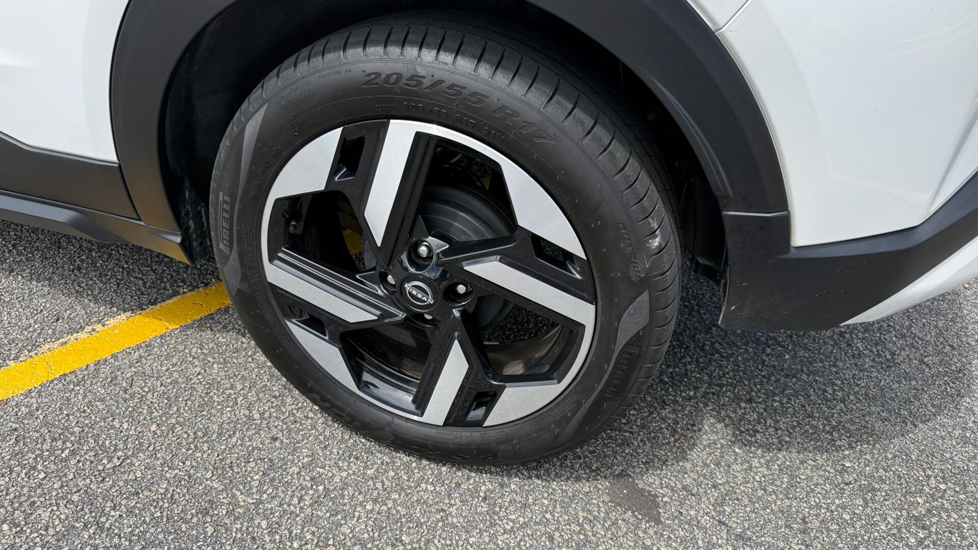 Roda de um carro com design moderno, mostrando o pneu e parte do veículo em uma superfície de estacionamento.