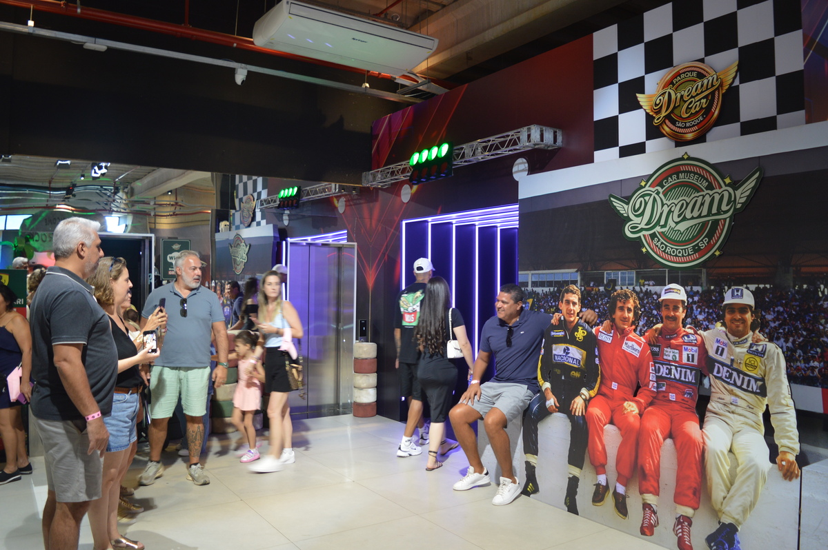 Visita ao Museu Dream Car em São Roque, com várias pessoas interagindo e currículos de pilotos de corrida expostos na parede.