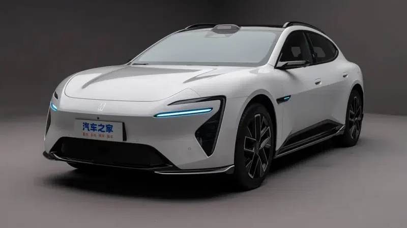 Um carro elétrico branco com design futurista, exibindo faróis de LED e detalhes em preto, posicionado em um ambiente neutro.