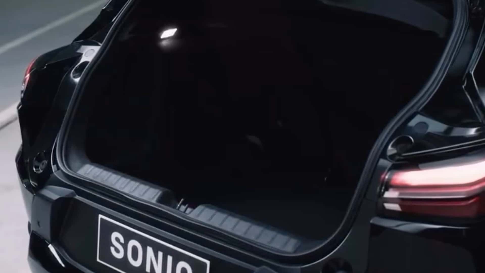 Visão detalhada do porta-malas de um carro preto, com iluminação interna suave e a placa do carro visível com a inscrição 'SONIQ'.