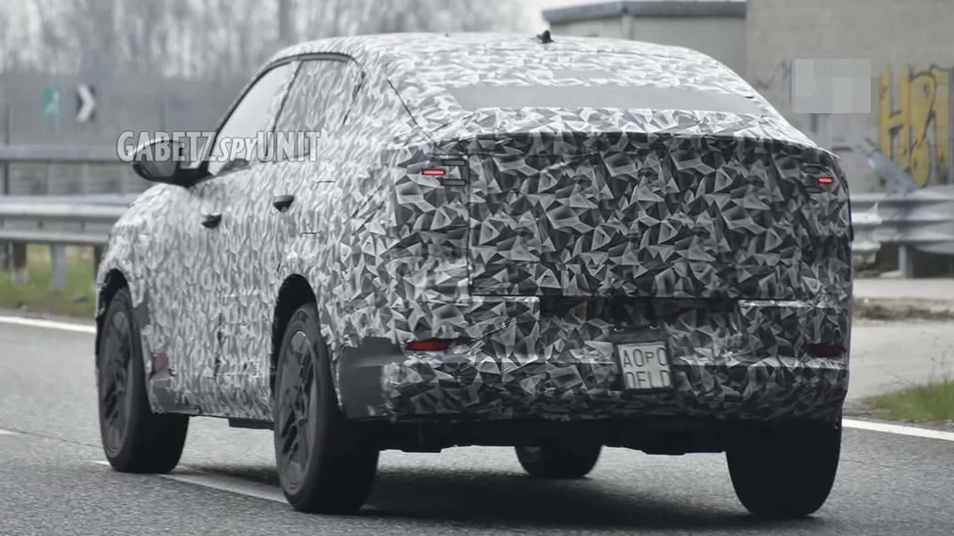 Um carro camuflado em teste rodando em uma estrada, com detalhes em preto e cinza.
