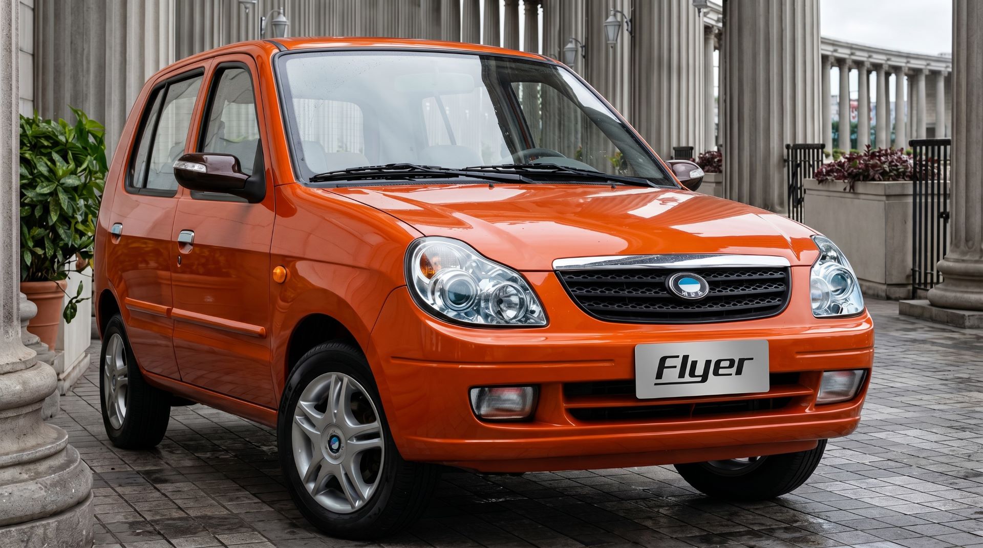 Carro compacto laranja modelo Flyer estacionado em um ambiente urbano com colunas e plantas ao fundo.