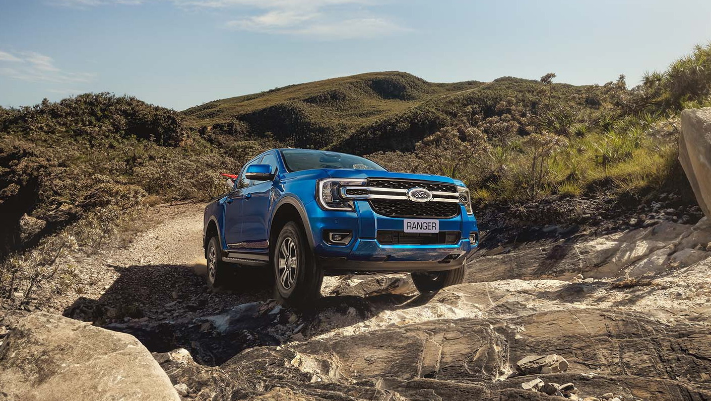 Picape Ford Ranger azul em uma trilha de terra e pedras, rodeada por vegetação montanhosa.