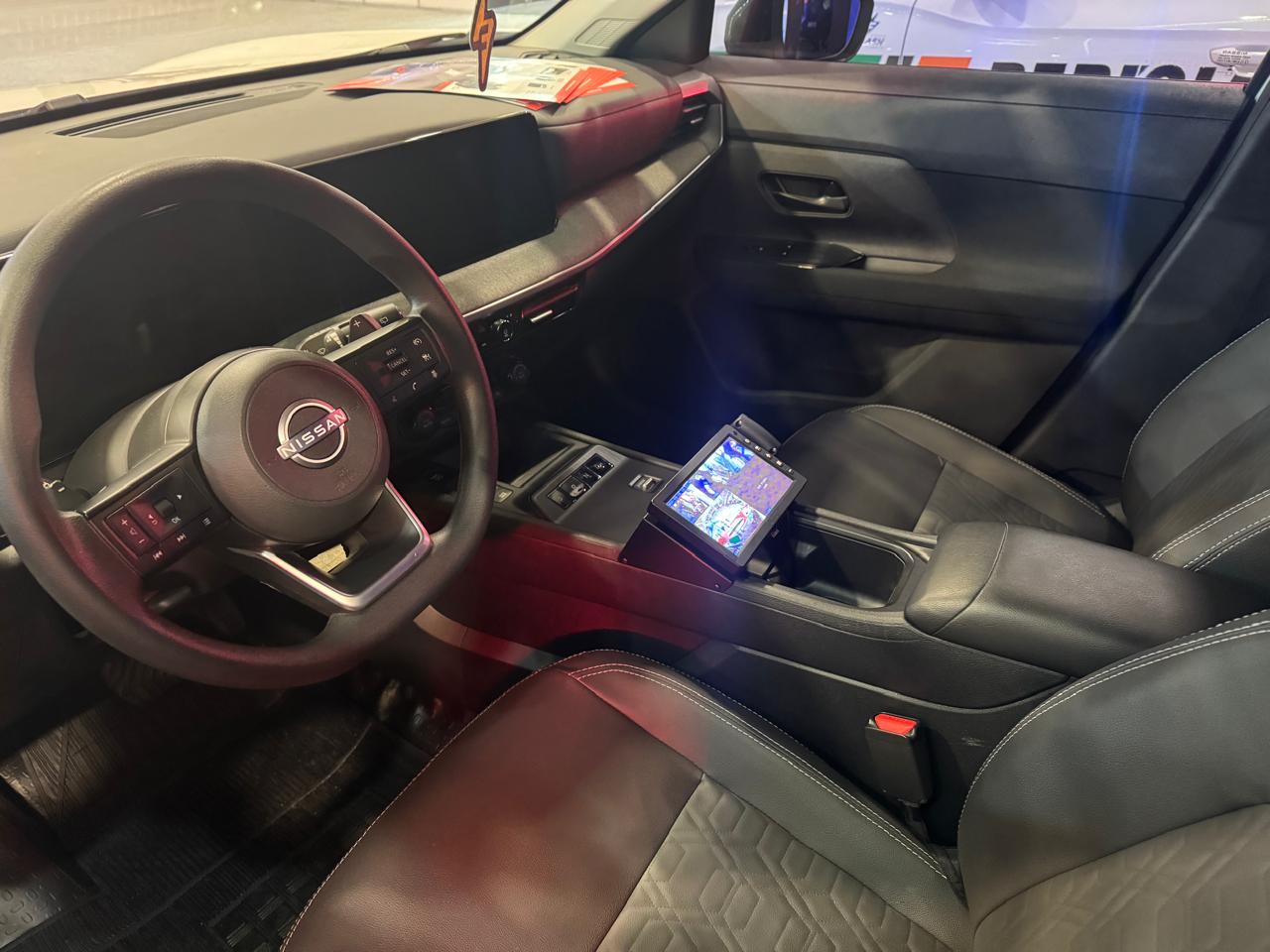 Interior de um carro Nissan, mostrando o volante, painel e porta-copos, com assentos em preto.