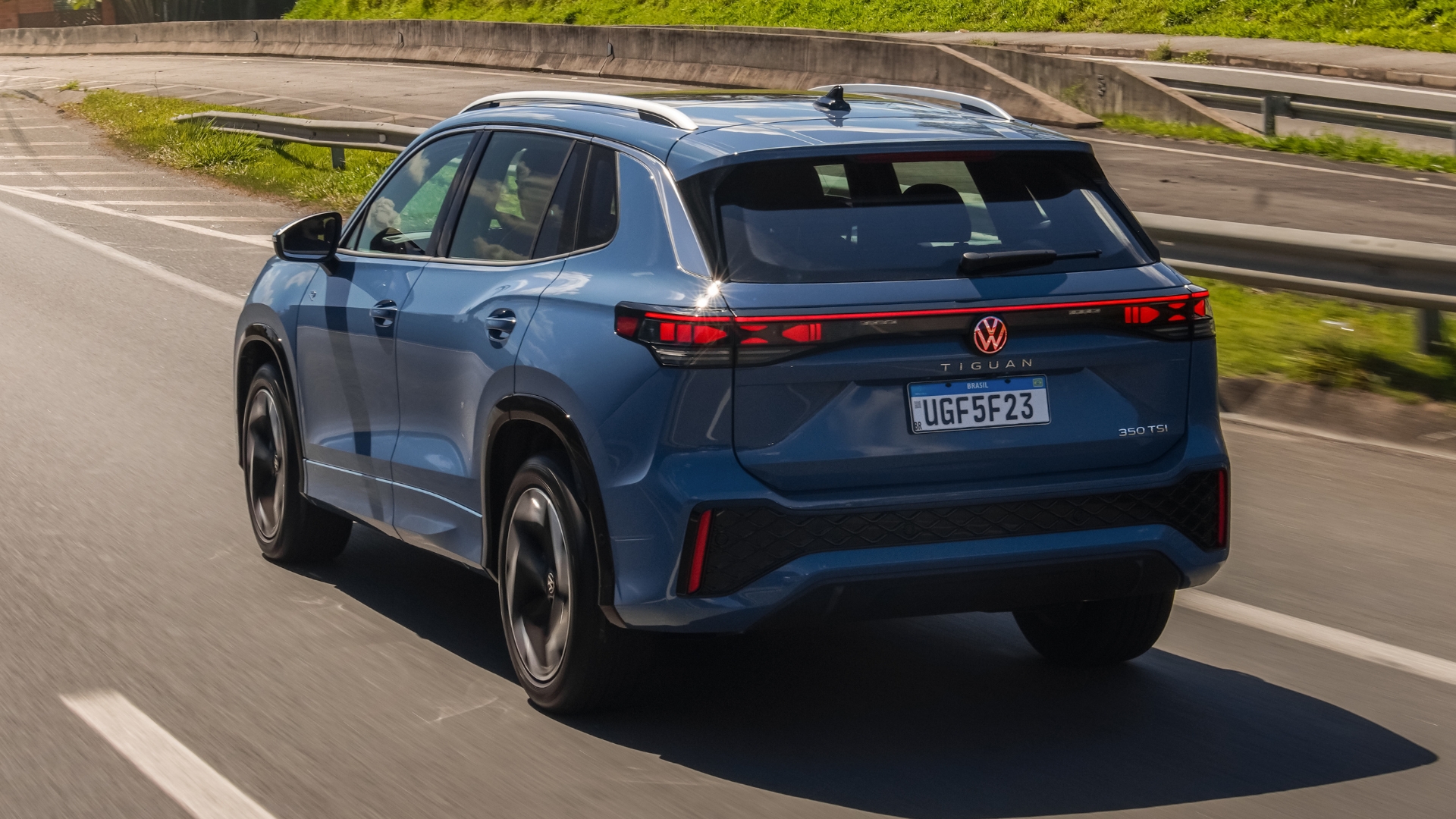 Um carro Volkswagen Tiguan azul em movimento em uma estrada, com foco na parte traseira e nos detalhes de iluminação.
