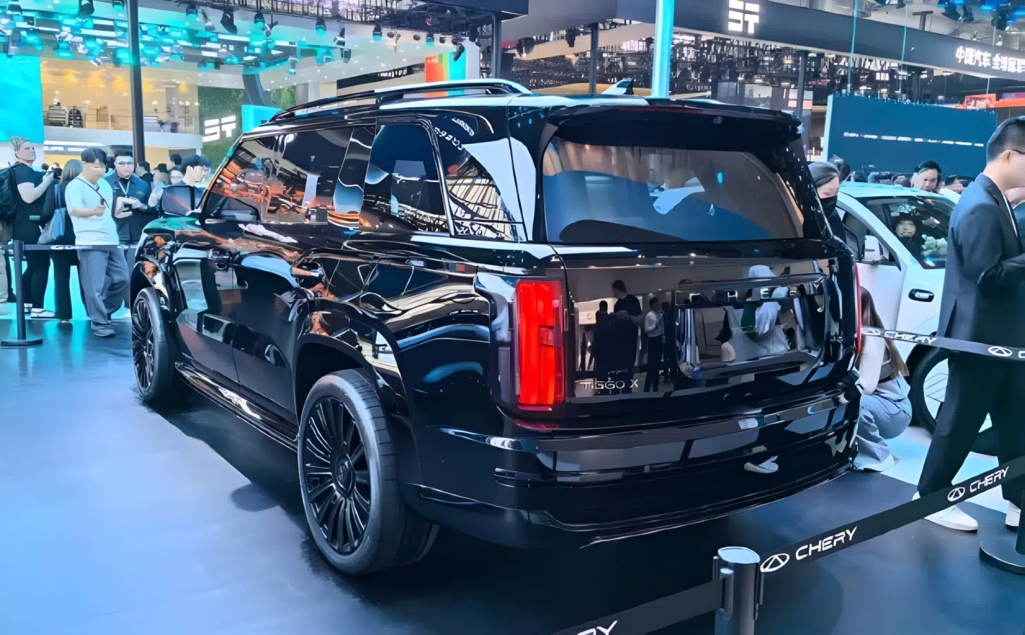 Imagem de um SUV preto exibido em um evento automotivo, mostrando sua traseira e detalhes do design, com público ao fundo.
