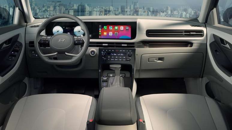 Interior de um carro moderno com volante, painel digital e console central. A vista externa mostra um horizonte urbano.