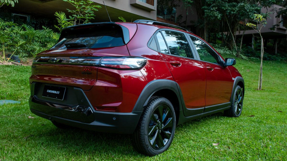 Veículo SUV da marca Chevrolet, na cor vermelha, visto de trás em um ambiente verdejante.