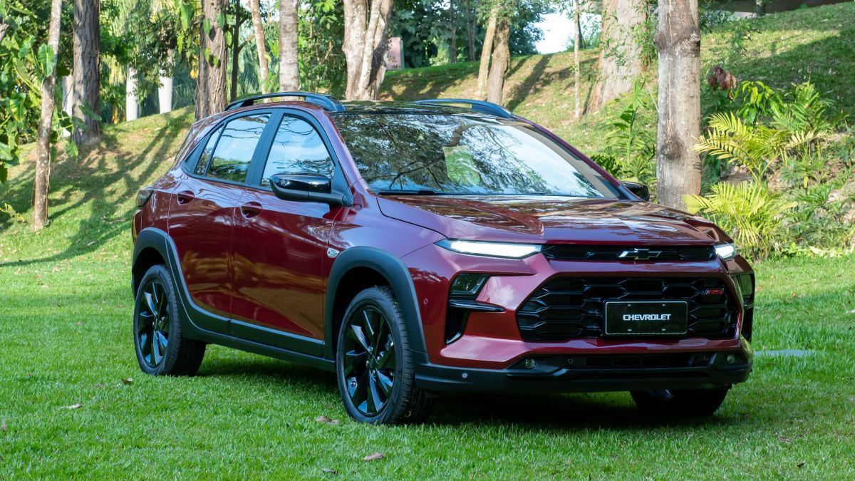 Veículo Chevrolet vermelho estacionado em um gramado, com árvores ao fundo.