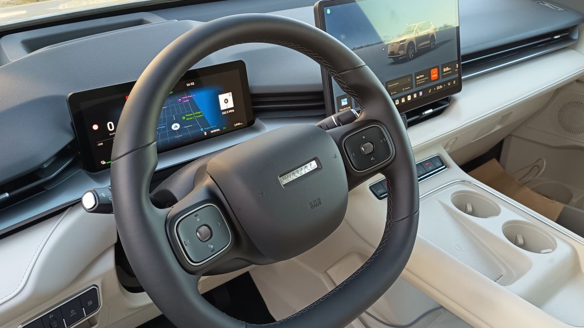 Interior de um carro elétrico com volante moderno, telas digitais mostrando informações do veículo e sistema de navegação.