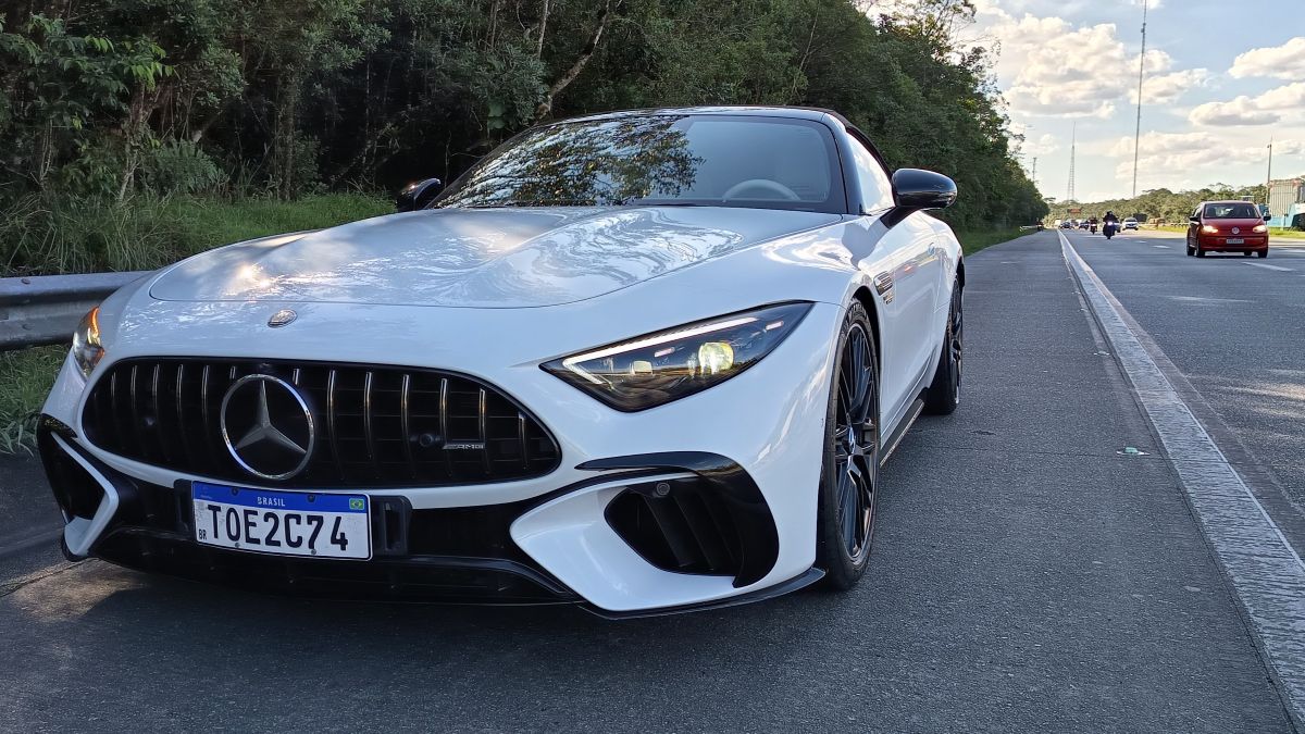 Carro esportivo branco da Mercedes-Benz estacionado na beira da estrada, com vegetação ao fundo.