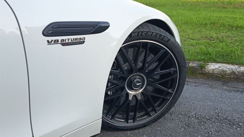 Detalhe do lado de um carro esportivo branco, mostrando a roda preta esportiva e o emblema V8 Biturbo da Mercedes.
