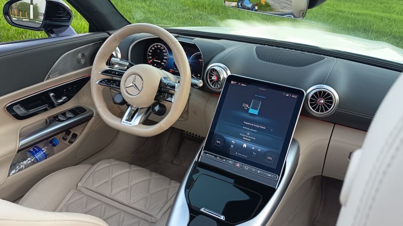 Interior de um carro de luxo com volante de couro claro, painel digital e tela central de controle. O assento e os detalhes são em bege, com um design sofisticado.