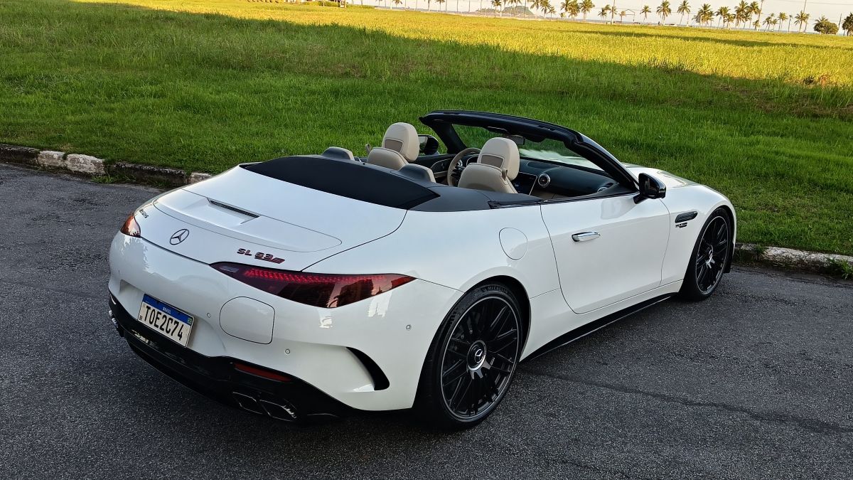 Um carro esportivo conversível branco Mercedes-Benz SL 63, estacionado em uma área verde com palmeiras ao fundo.