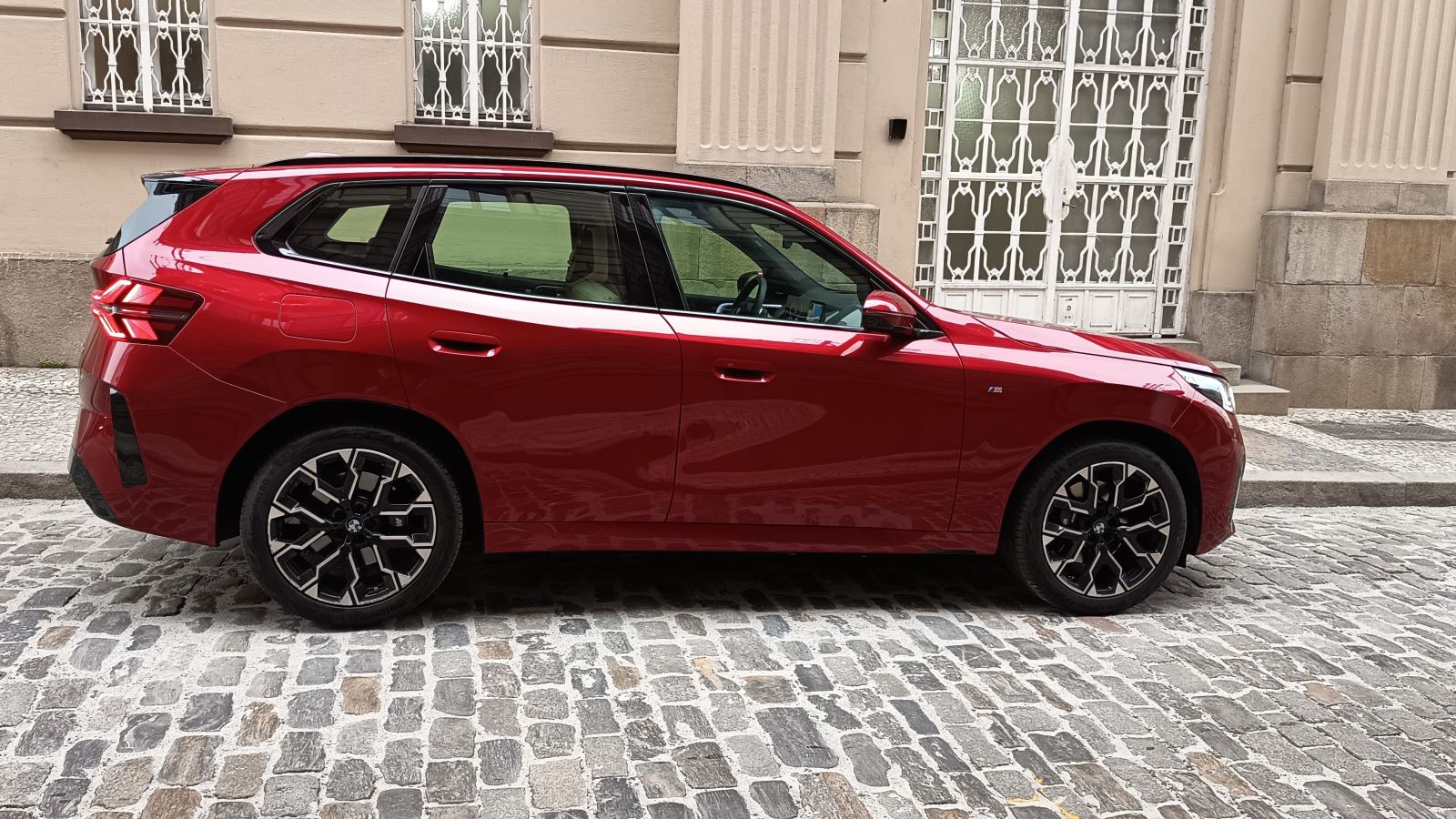 Carro vermelho estacionado em uma rua de pedras, com fachada de edifício ao fundo.